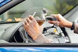 The driver is sitting behind the wheel and holding a bottle of alcoholic drink. Breaking the law and drinking alcohol while