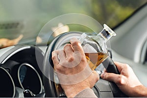 The driver is sitting behind the wheel and holding a bottle of alcoholic drink. Breaking the law and drinking alcohol while