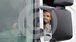 A driver sitting inside the semi-truck while looking at camera through the open window