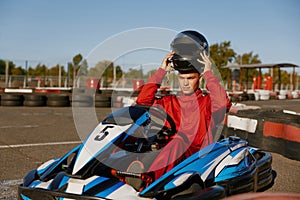 Driver taking off protective helmet while sitting at kart race car
