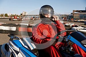 Driver taking off protective helmet while sitting at kart race car