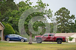 Driveway with Tesla Model 3 electric car and red lifted pick up truck