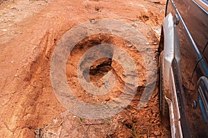 Driving 4wd vehicle on red dusty country road with big holes, detail on tire going over rough pothole terrain. Roads are in bad