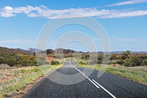 Driving across the MacDonnell ranges. Mountains at the background. Empty road, no cars, no signs. Green vegetation and bush on the