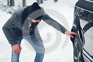Driving a car in winter. Man checks wheels on a snowy road before driving