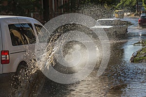 Driving cars on a flooded road during floods caused by rain storms. Cars float on water, flooding streets. Splash on the machine.