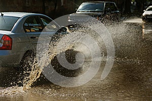 Driving cars on a flooded road during floods caused by rain storms. Cars float on water, flooding streets. Splash on the machine.