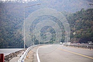 Driving on concrete road along the water reservoir dam in the area of rich natural forest tree mountain environment. Nature,