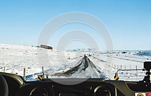 Driving on the country road in winter. Looking through car front windscreen, frozen road with snow covered and clear blue sky in I