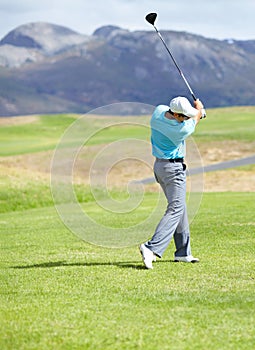 Driving it down the fairway. A young, fit male golfer following through after driving his ball down the fairway.