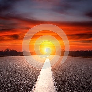 Driving on an empty asphalt road towards the sun