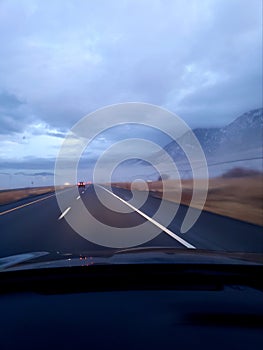 Driving on a highway road near mountains and stormy clouds