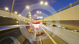 Driving in night city highway with traffic jam on road junction. Blurred timelapse. View from outside of the cabin