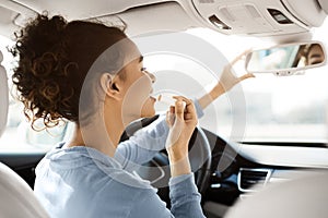 Driving safety concept. Afro woman doing makeup in car