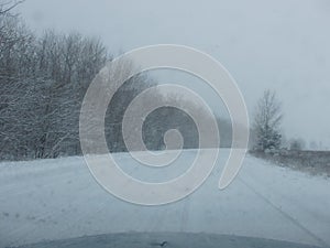 Driving in a snow storm. Poor visibility through the driver`s glass onto the road covered with snow and ice. Extreme weather in