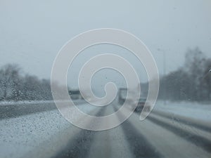 Driving in a snow storm. Poor visibility through the driver`s glass onto the road covered with snow and ice. Extreme weather in