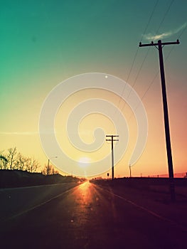 Driving into the sun on a road with telegraph poles