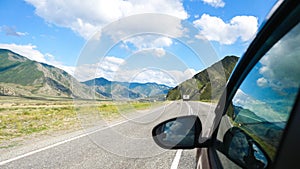 Driving view from side of car mirror mountain valley. Beautiful landscape of a road in the mountains on a sunny day