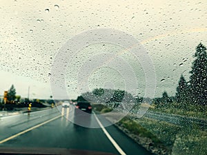 Drizzle on the windshield while driving in rain. Wet road and rainbow in the sky.