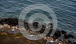 Drone aerial of empty beach umbrellas at a rocky coast in winter. Summer vacations