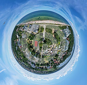 Drone aerial panoramic 360 degree view on sunny beach with sunbathers with windbreaks and towels at sea in touristic city