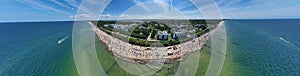 Drone aerial perspective and panoramic view on sunny beach with sunbathers with windbreaks and towels at sea in touristic city