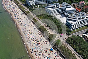 Drone aerial perspective view on sunny beach with sunbathers with windbreaks and towels at sea in touristic city