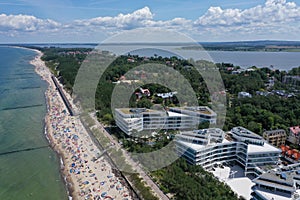 Drone aerial perspective view on sunny beach with sunbathers with windbreaks and towels at sea in touristic city