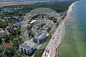 Drone aerial perspective view on sunny beach with sunbathers with windbreaks and towels at sea in touristic city