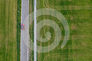 Drone aerial of Red car moving on a rural road. Countryside with green agriculture field.