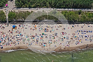 Drone aerial top down view on sunny beach with sunbathers with windbreaks and towels at sea in touristic city photo