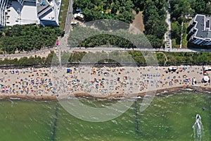 Drone aerial top down view on sunny beach with sunbathers with windbreaks and towels at sea in touristic city