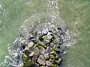 Drone aerial view directly over a rock jetty with ocean water pounding thee boulders