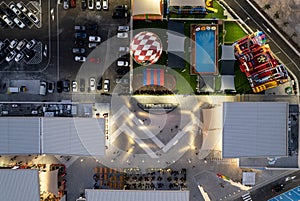 Drone aerial view of parking lots with cars and entertainment park at night. Bright crowded shopping mall