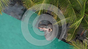 Drone aerial view of slim young woman in beige bikini and straw hat relaxing in luxury swimming pool.Vacation concept.