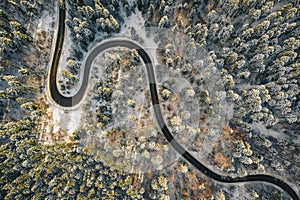 Drone aerial view of a winding road in the middle of the forest with snow on trees