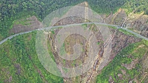 Drone approaches mountain highway curve on steep cliff