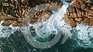 Drone of azure waves meeting rugged tropical coastline. Aqua ocean swirls, crashes into jagged rocks, creating white