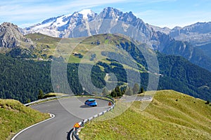 DRONE: Blue rally car drives towards a sharp turn in beautiful sunny Dolomites.