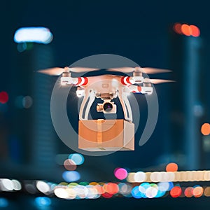 Drone with camera against nighttime cityscape, carrying rectangular box