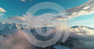 Drone camera filming through the clouds above the snowy mountains of Central Asia on the sunset