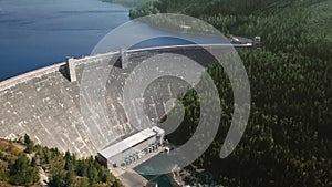 Drone camera moving reservoir in front of a dam at the foot of wooded mountains