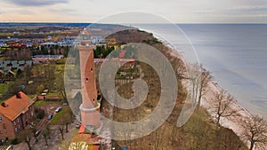 A drone captures Gaski beach, West Pomeranian Voivodeship, Poland, featuring a red brick lighthouse, Baltic Sea, sandy shore,