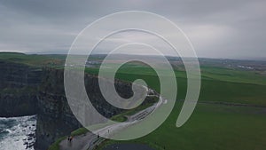 Drone capturing video from the air of amazing tourist place cliffs of moher , tourist exploring the landscape.