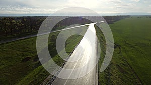 Drone descends above wet asphalt road for cars between sown fields