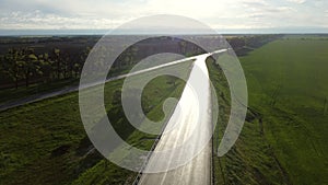 Drone descends above wet asphalt road for cars between sown fields