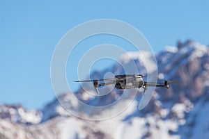 Drone with digital camera flying over winter landscape with snow covered mountains and trees. White remote controlled