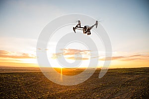 Drone with digital camera flying in sky over field on sunset