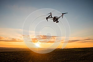 Drone with digital camera flying in sky over field on sunset