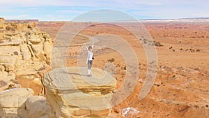 DRONE: Excited female traveler standing atop a boulder overlooking the canyon